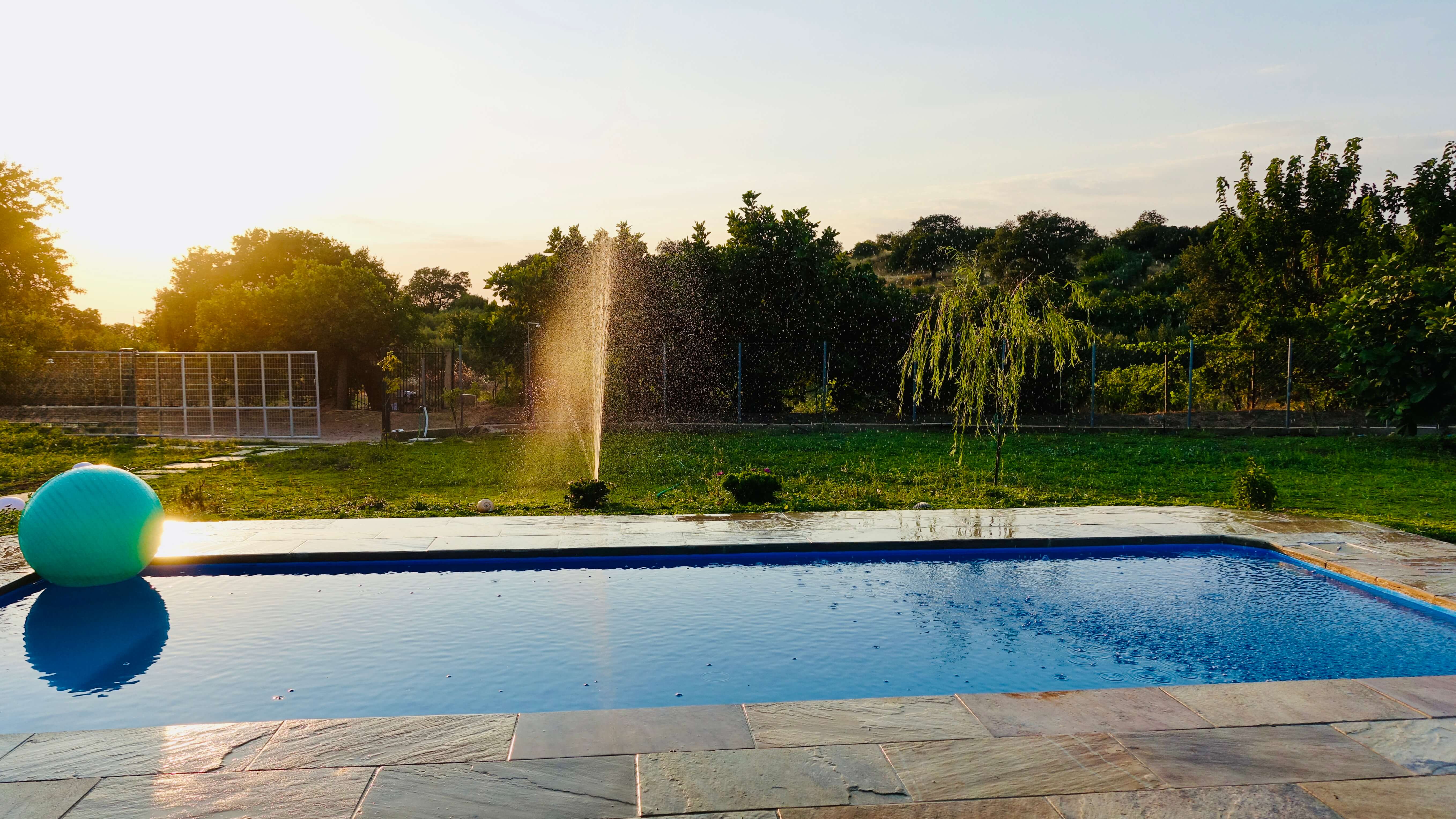 Private swimming pool at sunset with garden sprinkler and low sun through the trees