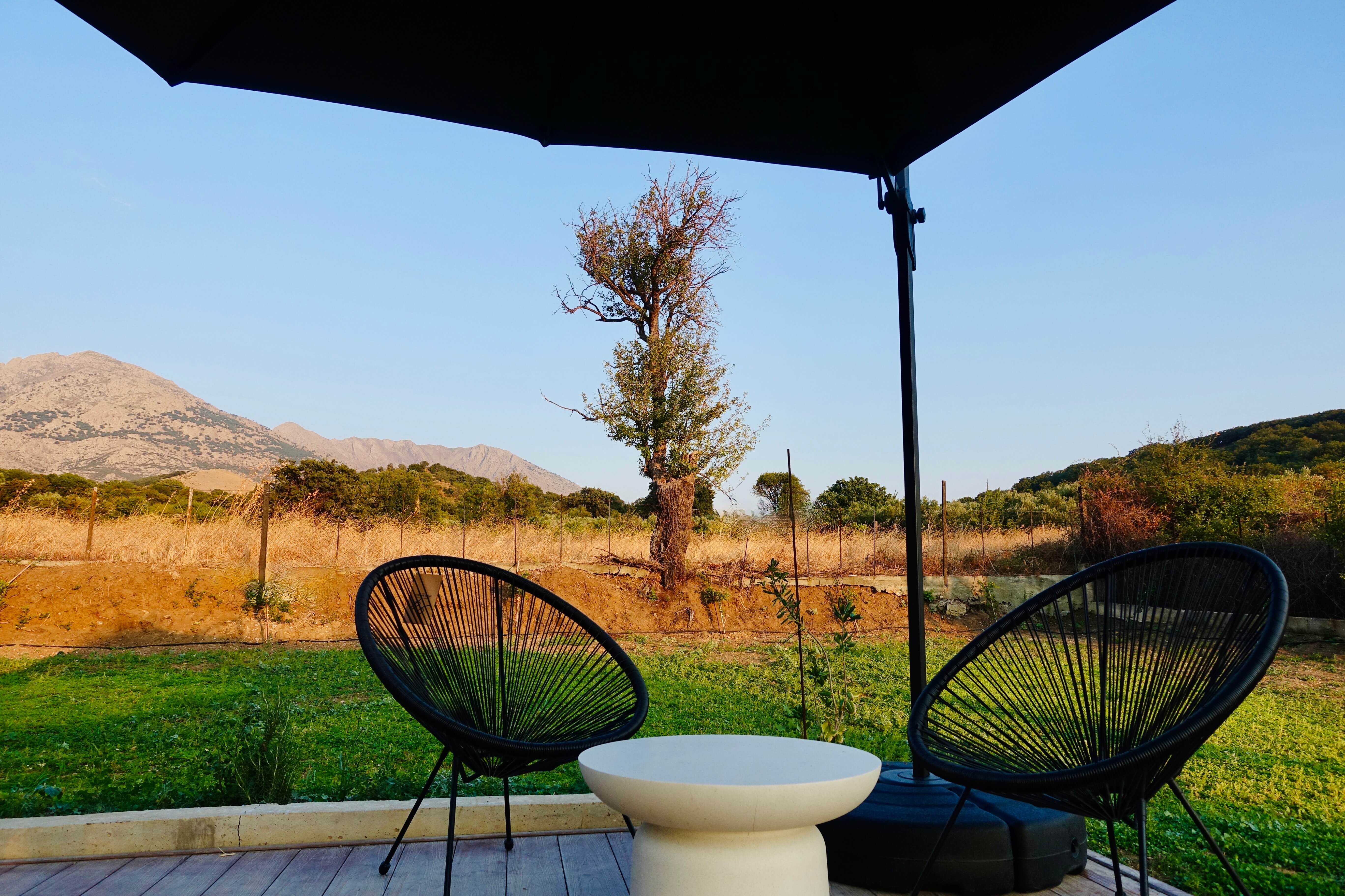 Two chairs and a side table on the shaded terrace looking out to Mount Fengari and open countryside
